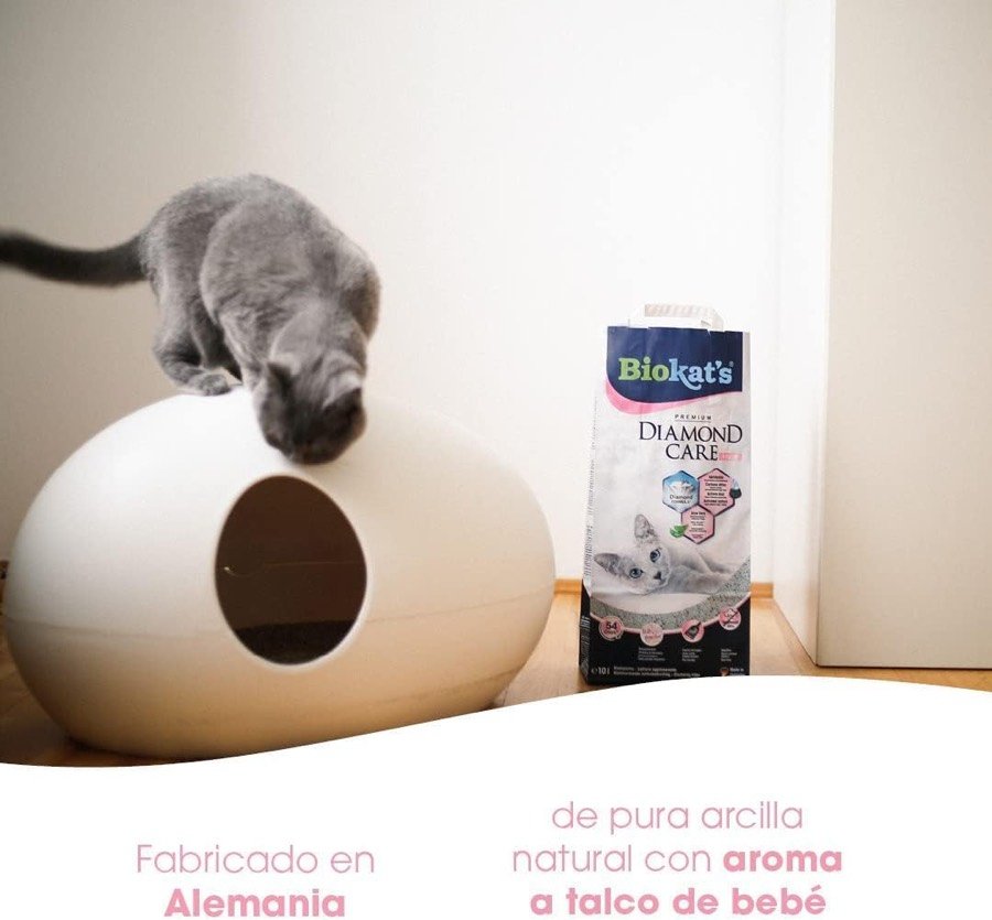 Ver imagen 2 de 6: Gato gris asomado a un arenero cerrado blanco junto al saco Biokat's, con los rótulos «Fabricado en Alemania» y «aroma a talco de bebé»
