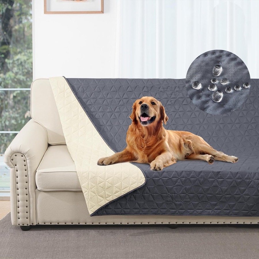 Golden retriever tumbado sobre la manta Taiyang gris acolchada que cubre un sofá blanco, con una esquina doblada que enseña el reverso beige y gotas de agua en detalle