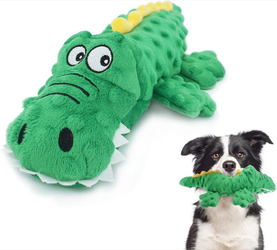 Cocodrilo de peluche ZENVALY verde con cresta amarilla, junto a un border collie que lleva otro igual en la boca